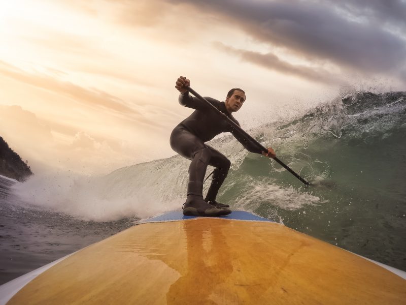 Adventurous man stand up paddle boarding a wave in the ocean.