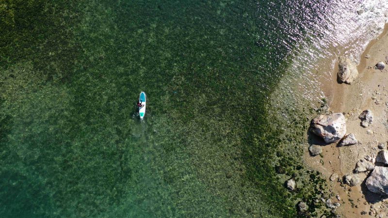 Aerial photo of a lady paddling boarding in calm translucent clear water.