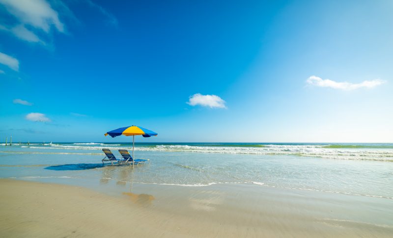 Beautiful sunny day of two beach chairs and an umbrella in shallow water at Daytona Beach in Florida.