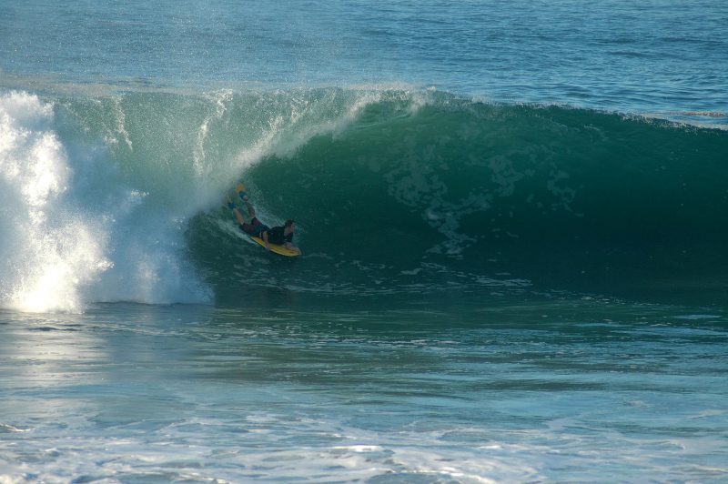 Man with fins on a boogie board in the middle of breaking wave.