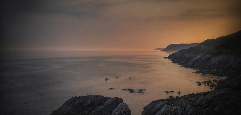 Pretty zoomed out sunset photo capturing three paddle boarders near the shores of mountains.