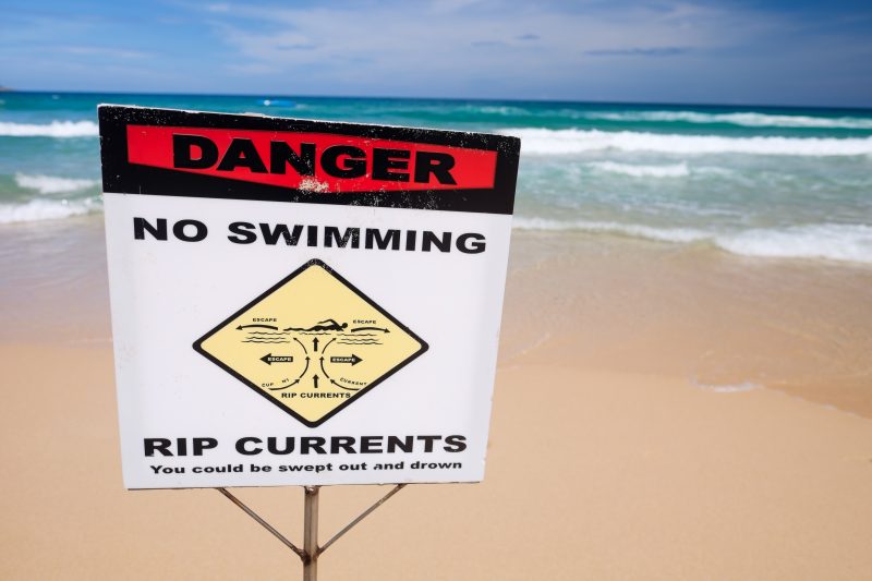 No swimming warning sign due to rip currents on the beach.