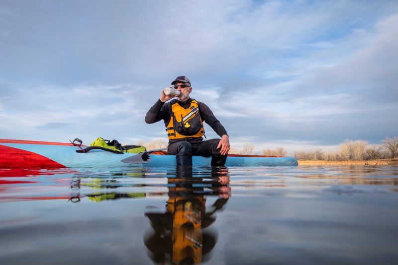 Senior male drinking water recovering from a workout on a stand up paddle board.