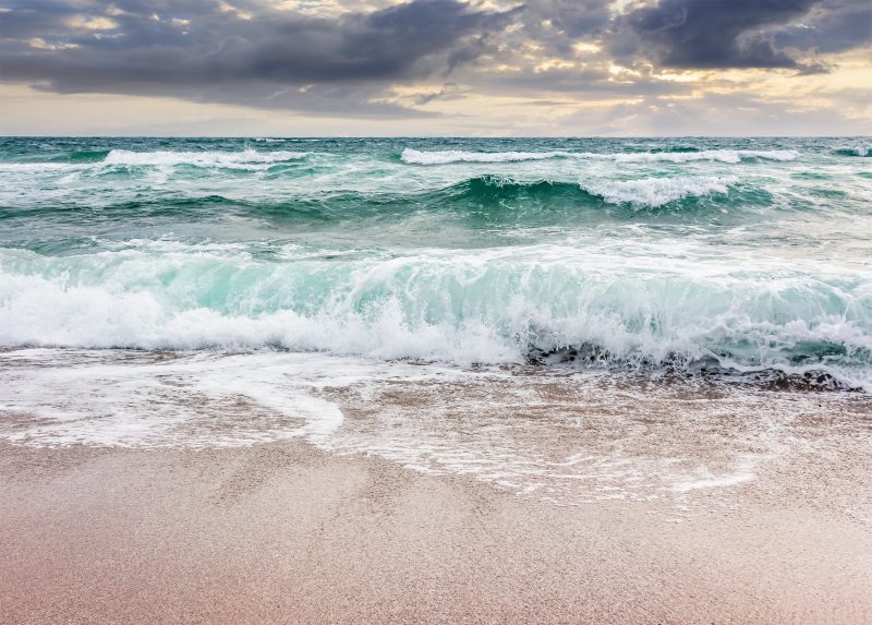 Waves crashing on beach with dark clouds above.