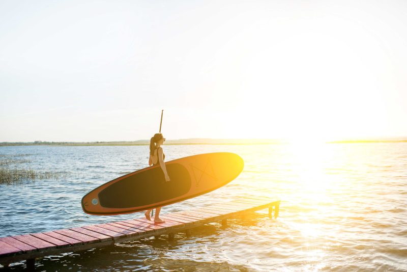 Woman Launching Paddle Board on Lake.