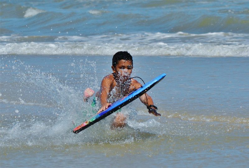 Young boy at shore break catching his boogie board with his leash.