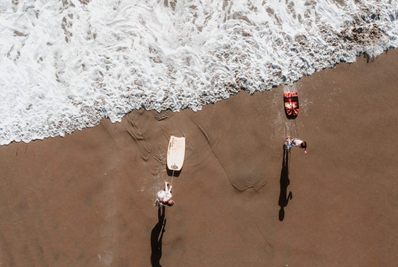 Two kids with their boogie boards by the shoreline.