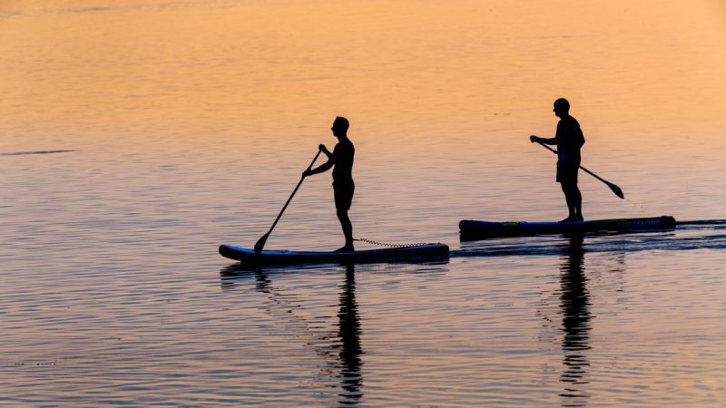 Two individuals stand up paddling boarding during sunset.